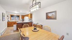 Una cocina moderna con armarios de madera, un refrigerador blanco y una zona de comedor con mesa y sillas de madera.