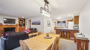 Una sala de estar moderna con chimenea, un comedor y una cocina con armarios de madera y una ventana.