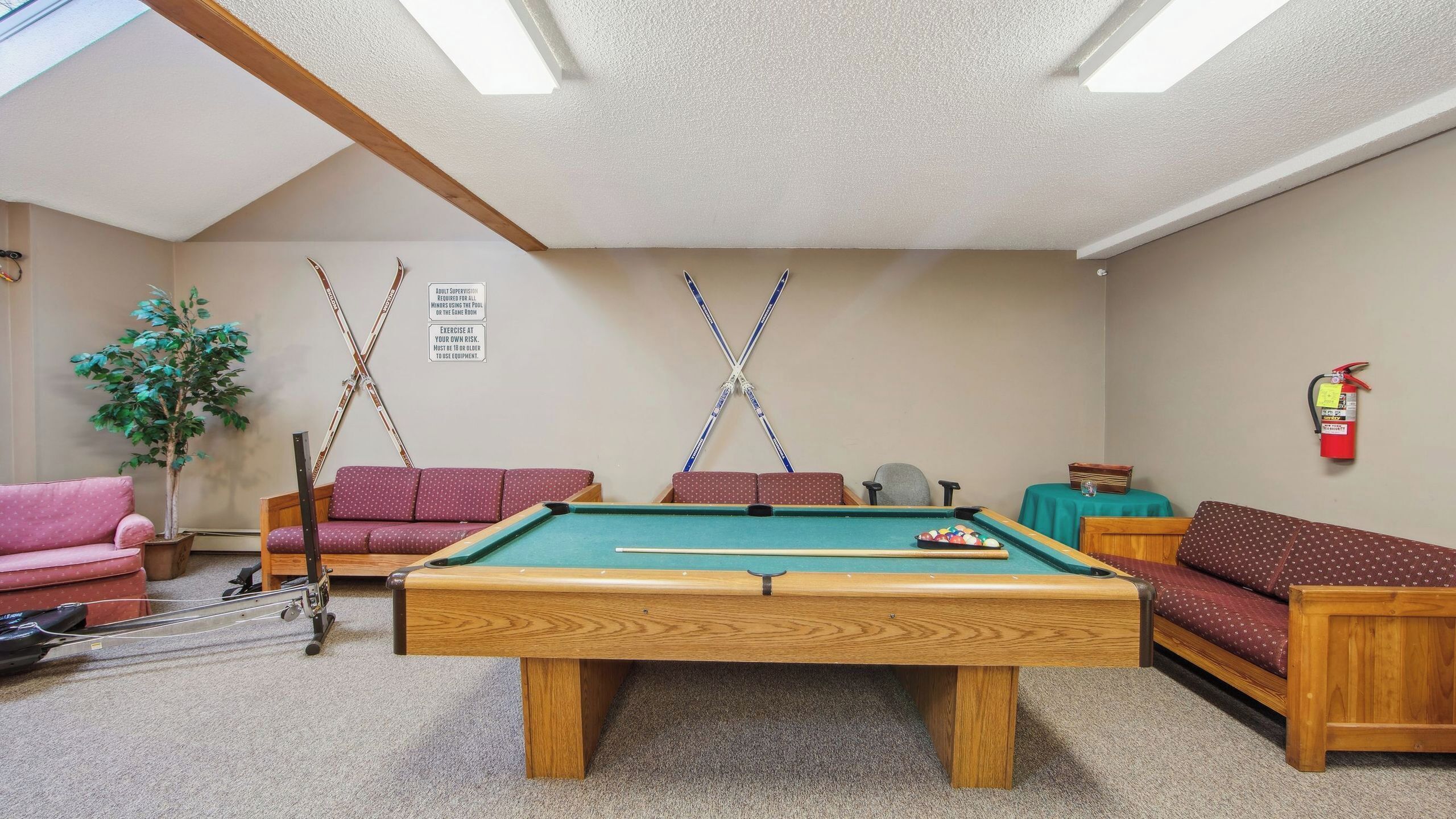 A pool table in a room with a ceiling fan, a fire extinguisher, and two sofas.