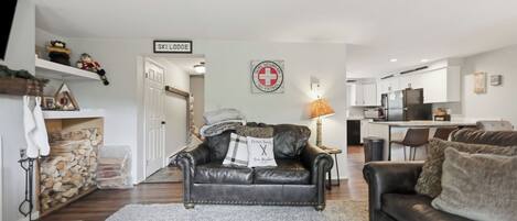 A living room with a fireplace, a couch, a coffee table, and a kitchen in the background.
