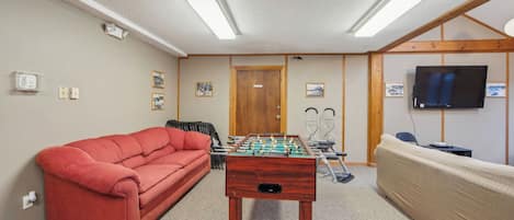 A room with a red sofa, a foosball table, a television, and a wooden door.