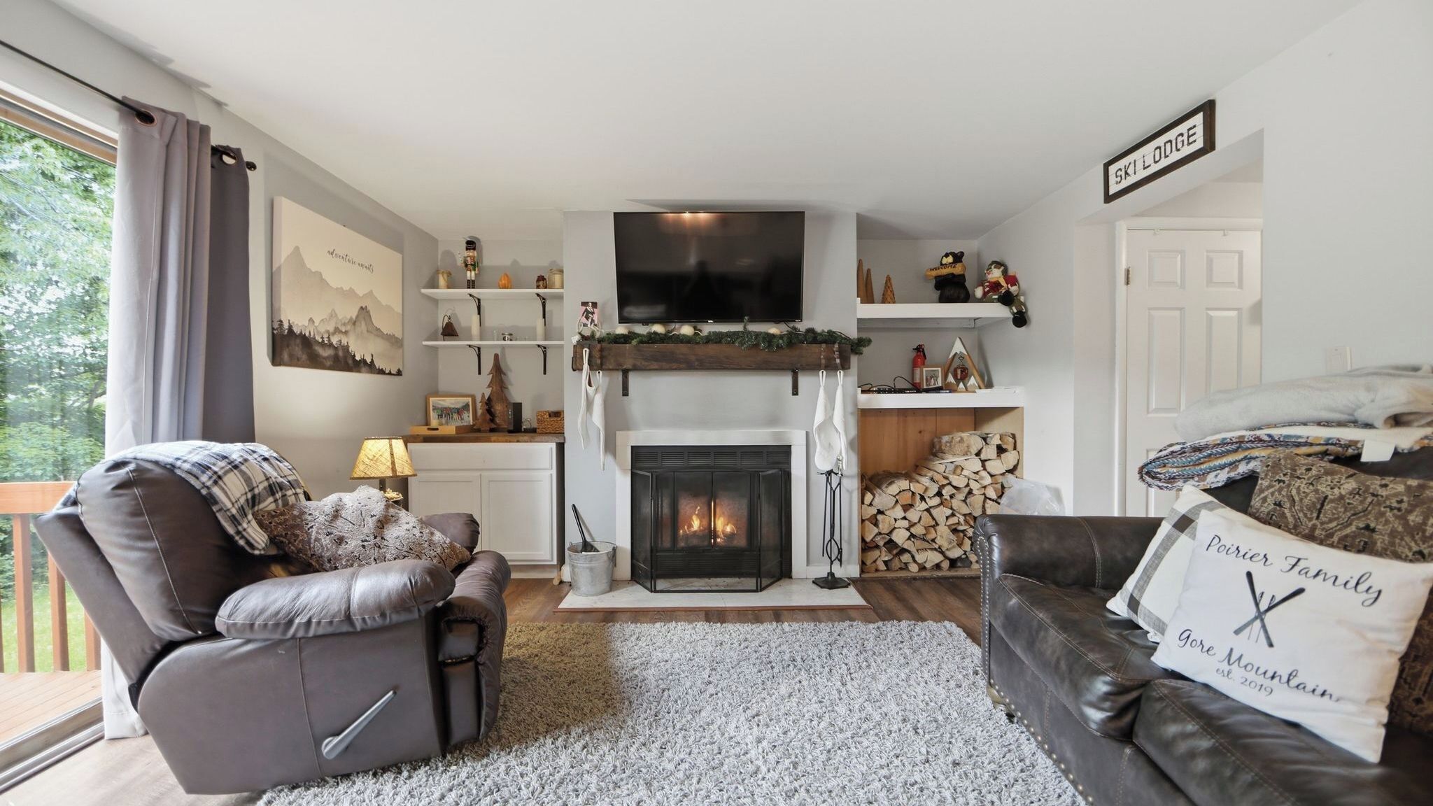 A living room with a fireplace, a sofa, a television, and a sign that reads 'SKILODGE'.