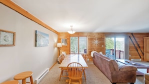 A wooden cabin interior with a dining table, chairs, a sofa, a lamp, and a large window. - Echo by Avantstay Sauna + Indoor Pool + Fireplace Near Gore Mountain (North Creek)