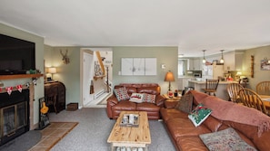 A living room with a fireplace, a sofa set, a coffee table, and a kitchen area in the background. - Lower Sleighride by Avantstay Heated Pool + Rec Lounge Near Gore (North Creek)