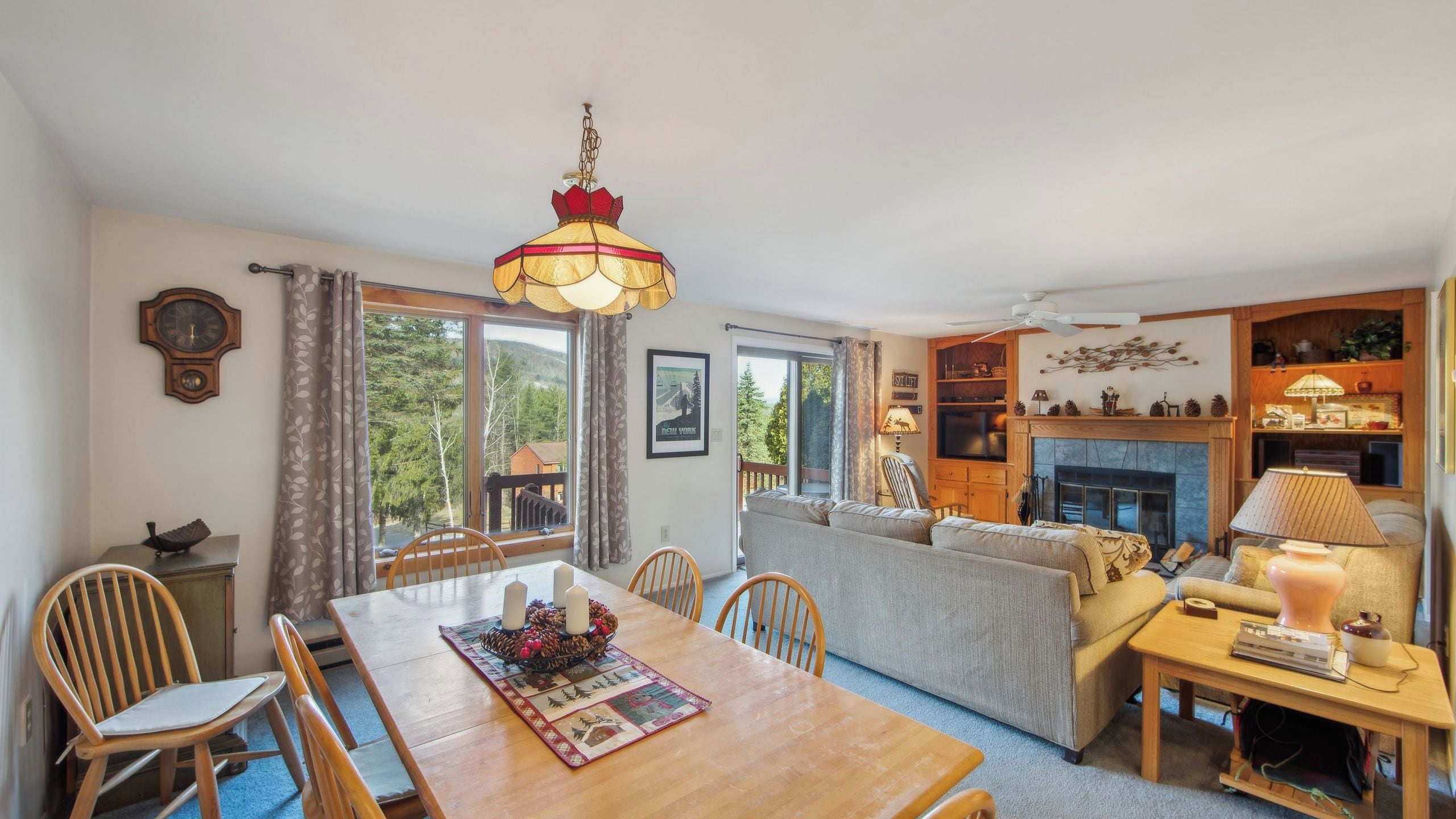 A cozy living room with a fireplace, a dining area with a wooden table, and a large window offering a view of the outdoors.