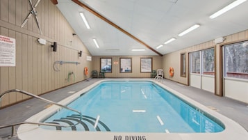 An indoor swimming pool with a 'NO DIVING' sign, lifebuoys, and a lifeguard warning sign.
