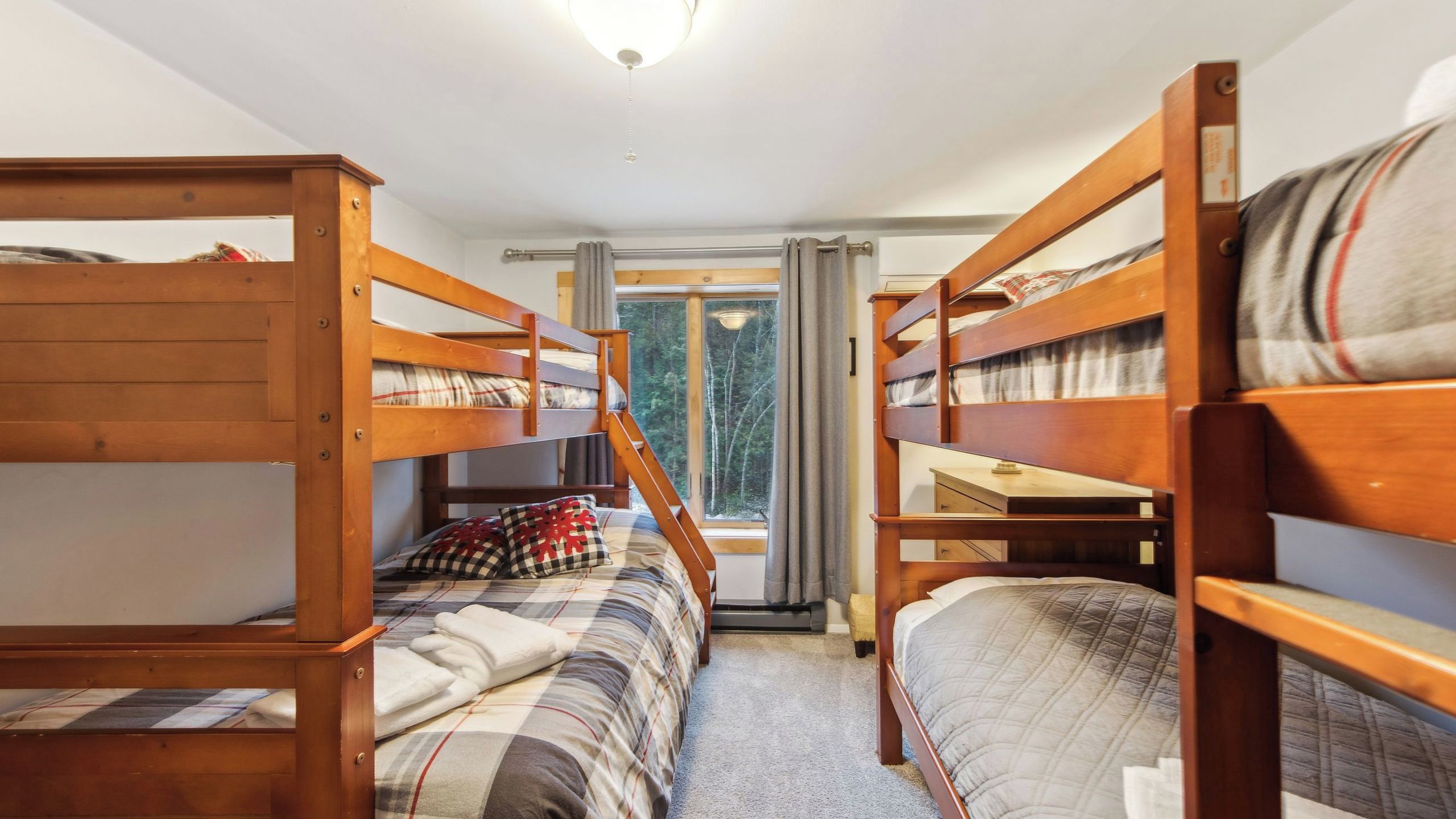 Een kamer met stapelbedden, een raam met gordijnen en uitzicht op bomen.
