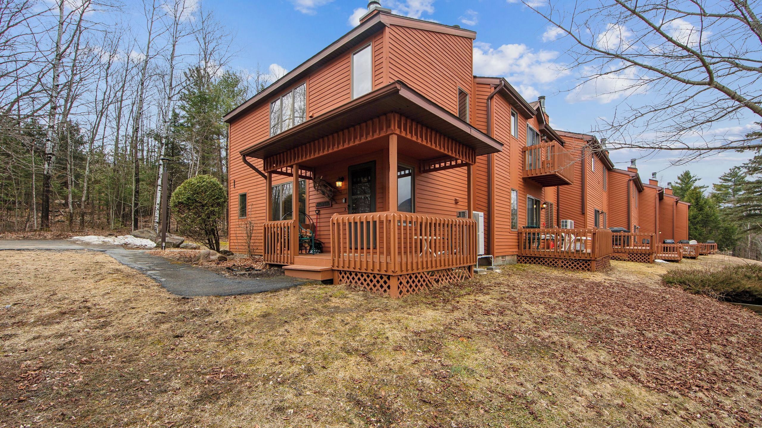 A two-story wooden cabin with a porch, a covered deck, and a large window.