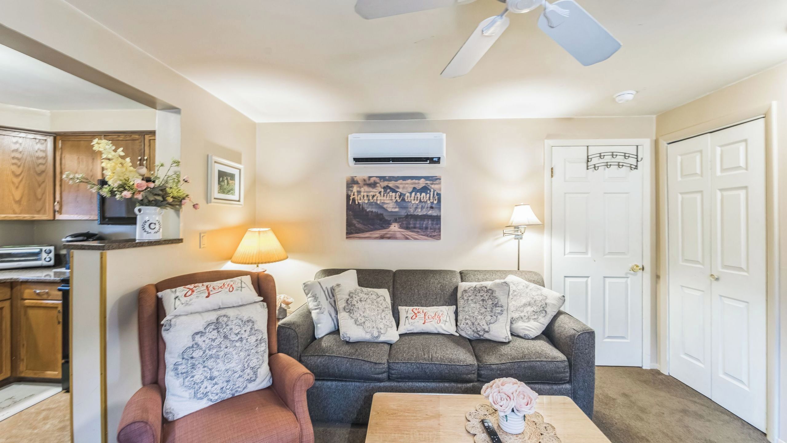 A living room with a sofa, armchair, and coffee table, a kitchen area, and a door.