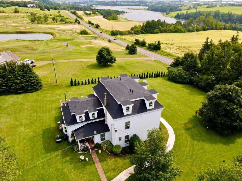 Une grande maison blanche, dotée d’un toit sombre, entourée d’une pelouse bien entretenue et d’un terrain de golf.