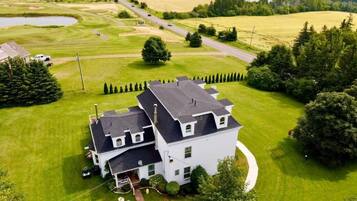 A large white house with a dark roof, surrounded by a well-maintained lawn and a golf course.