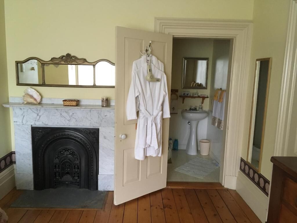 A room with a fireplace, a mirror, a sink, and a door leading to another room.