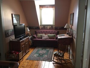 Ein kleiner Raum mit Fernseher, einer Couch, einem Schaukelstuhl und einem Fenster mit Jalousien.