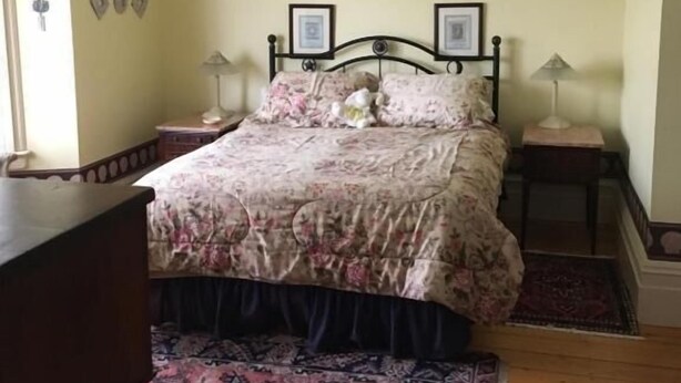 A bedroom with a bed, two bedside tables, a ceiling fan, a rug, and a picture on the wall. - New Glasgow Inn (New Glasgow)