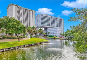 A high-rise hotel with a water feature in front, surrounded by greenery and a clear sky. - N Hampton 222 in Kingston, Oceanfront, Pool, Beach (Myrtle Beach)