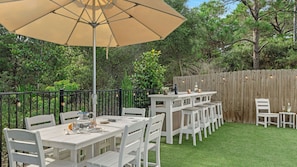 Eine Terrasse im Freien mit Tisch und Stühlen, einem großen Sonnenschirm und einem Holzzaun.