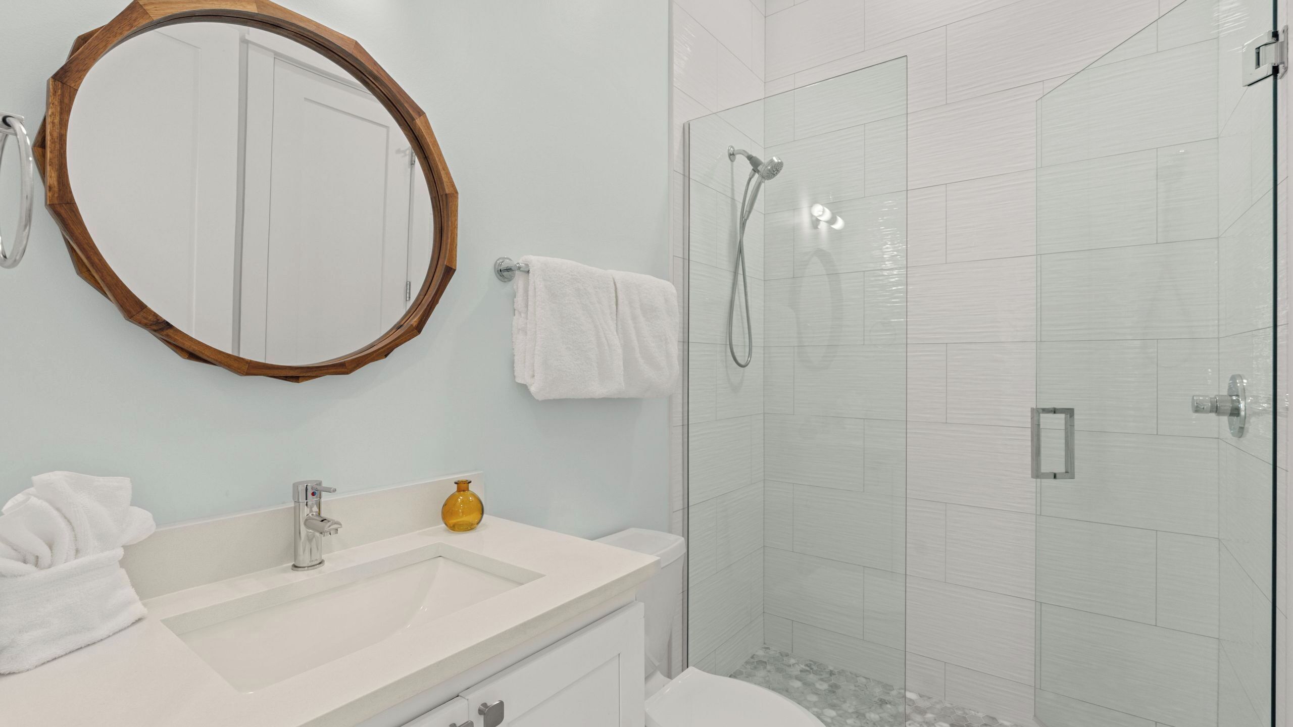 A bathroom with a sink, mirror, towel rack, and shower.