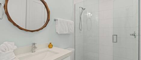 A bathroom with a sink, mirror, towel rack, and shower.