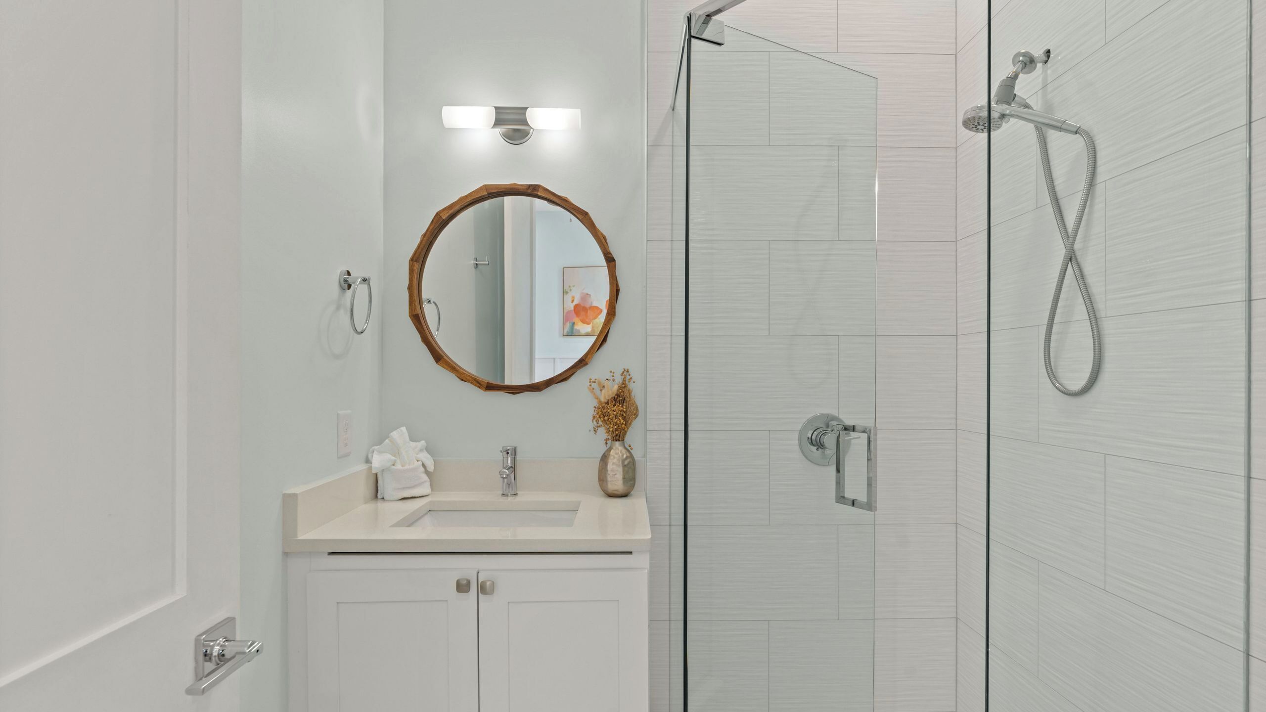 A modern bathroom with a sink, mirror, towel rack, and shower.