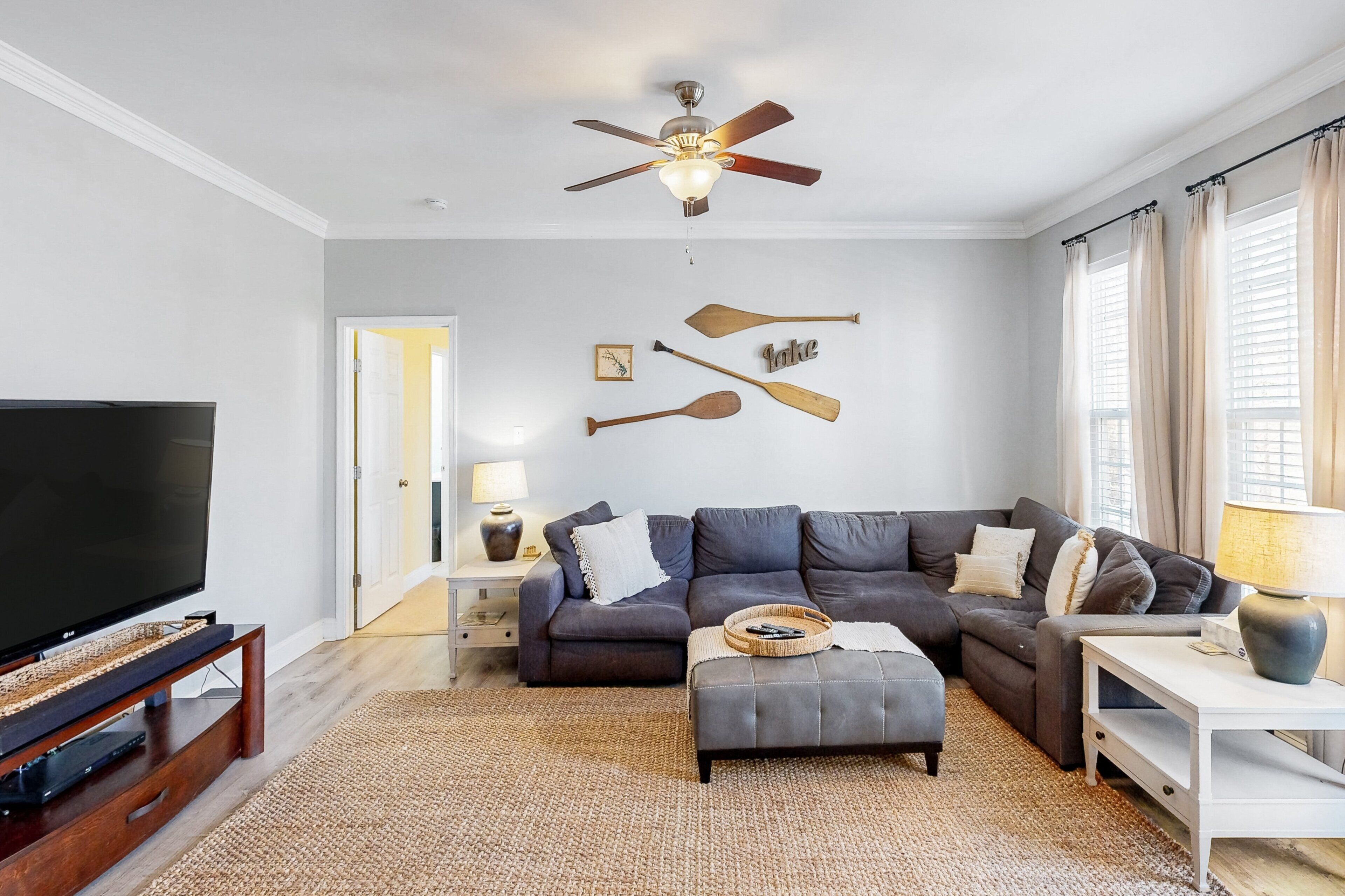 A living room with a television, sofas, a ceiling fan, and wall-mounted paddleboards.