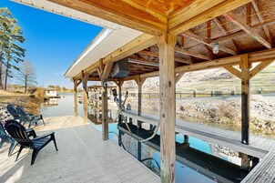 A covered deck with chairs, a pool, and a view of a lake and hills.