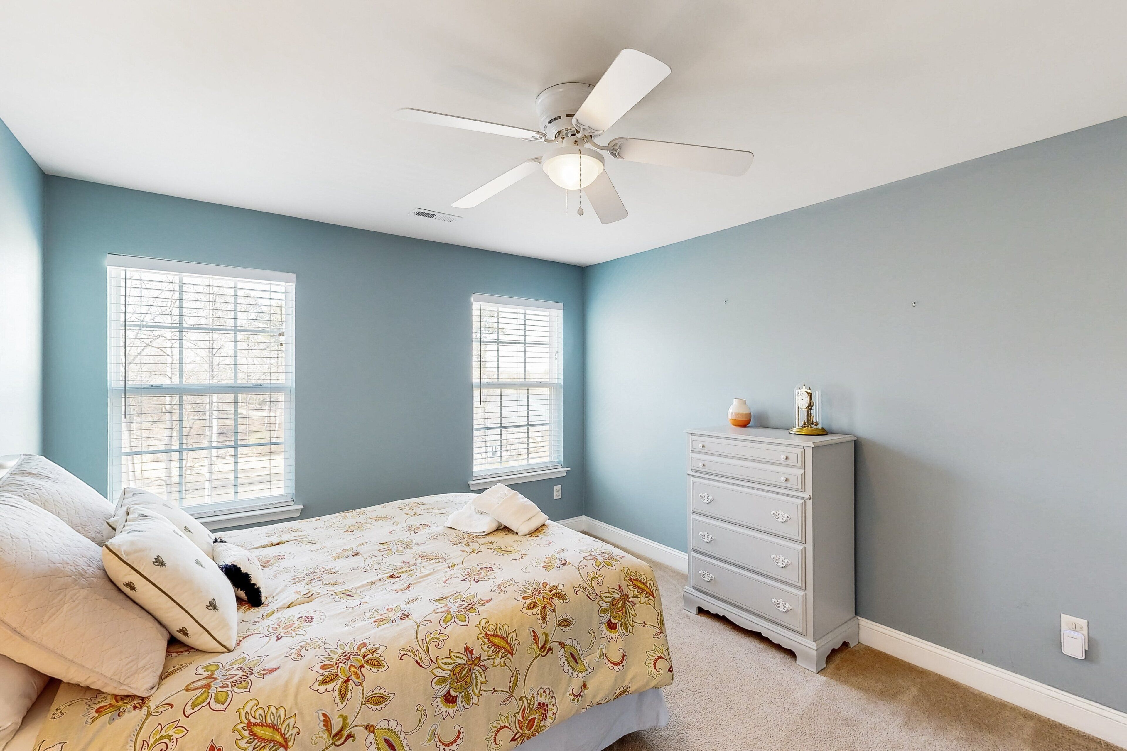 A bedroom with a bed, two windows, a dresser, and a ceiling fan.