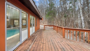 Une terrasse en bois avec des portes vitrées donnant sur une piscine, le tout entouré d’une forêt.