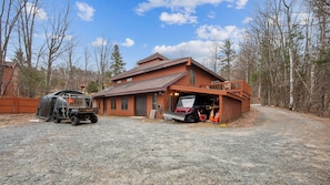 Une cabane en rondins à deux étages, avec une allée en gravier, un véhicule abrité et un chariot de golf.