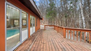 A wooden deck with glass doors leading to a pool, surrounded by a forest. - Cloud by Avantstay Sauna + Indoor Heated Pool + Game Lounge Near Gore Mtn (North Creek)