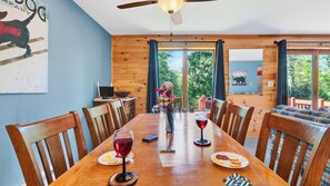 Een houten eettafel met stoelen, een plafondventilator en uitzicht op het landschap door grote ramen.