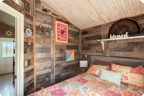 Un dormitorio con panel de pared de madera, cama con ropa de cama floral, un cartel con la palabra 'blessed' y una obra de arte acolchada.