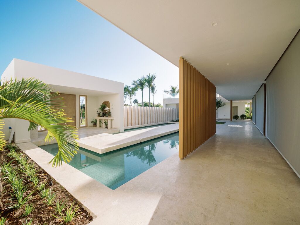 Un espace piscine moderne avec une piscine à eau claire, une clôture en bois et un chemin menant à un bâtiment.
