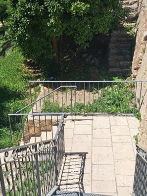 Ein gepflasterter Weg mit Metallgeländern, umgeben von Grünpflanzen und einer Steinmauer.