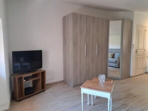 Ein Zimmer mit Fernseher auf einem Holzständer, einem kleinen Tisch mit einem Glas und einem Kleiderschrank mit Schiebetüren.