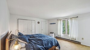 A bedroom with a bed, a bedside lamp, a heater, a window with curtains, and a door with a sign. - North Side by Avantstay Sauna + Heated Pool + Rec Center Minutes to Gore Mtn (North Creek)