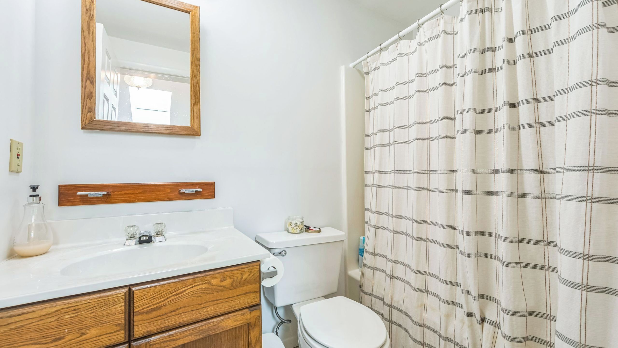 Un baño con tocador de madera, un espejo, un inodoro y una cortina de ducha.