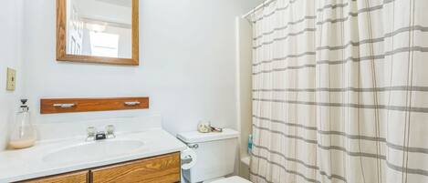 Un baño con tocador de madera, un espejo, un inodoro y una cortina de ducha.