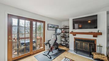 A room with a large sliding glass door, a stationary exercise bike, a fireplace, and a mounted TV.