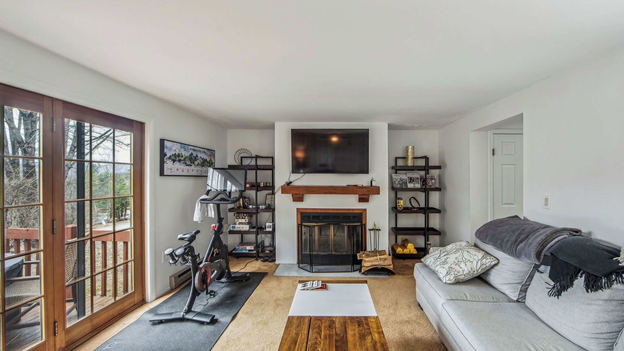 A living room with a fireplace, a sofa, a treadmill, and a large window.