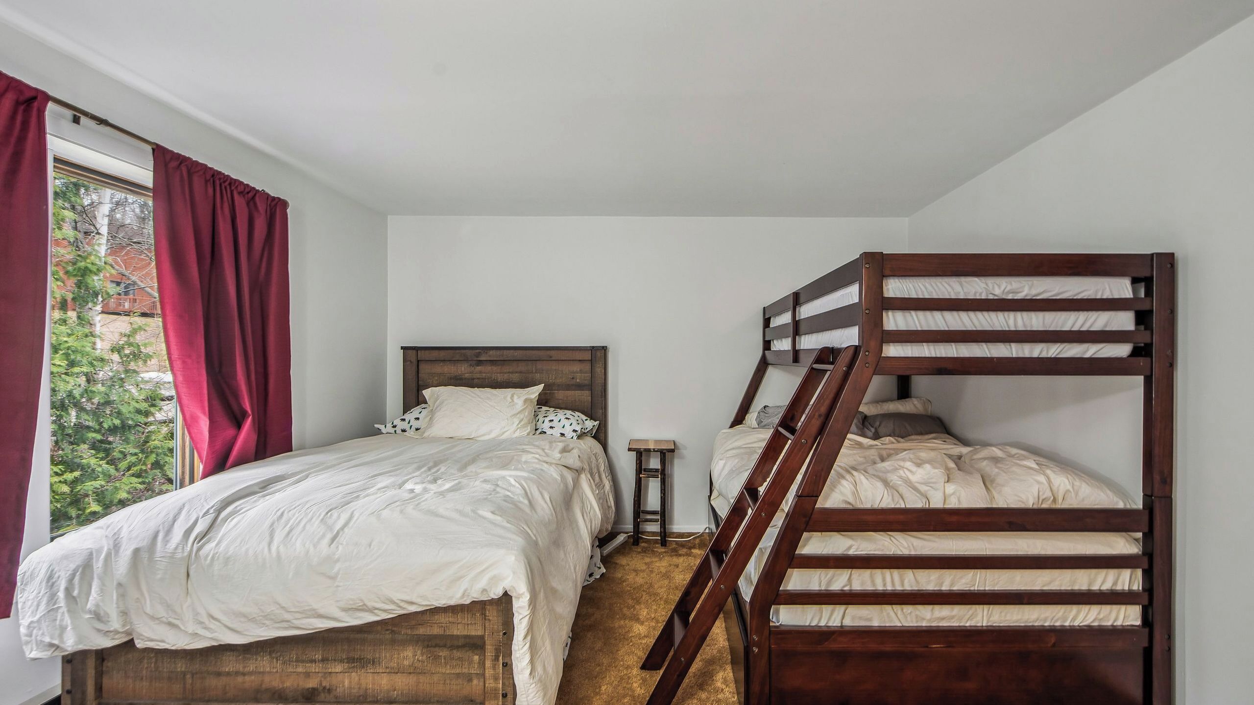 Quarto com uma cama de solteiro, uma cama beliche, uma mesinha e uma janela com cortinas.