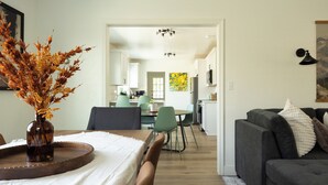 A modern living room with a dining area, a kitchen in the background, and a hallway leading to another room. - Game Day Getaway - 4BR/3BA, Sleeps 10, Walk to WSU (Pullman)