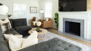 A living room with a sofa, armchair, coffee table, fireplace, TV, and a framed picture on the wall. - Game Day Getaway - 4BR/3BA, Sleeps 10, Walk to WSU (Pullman)