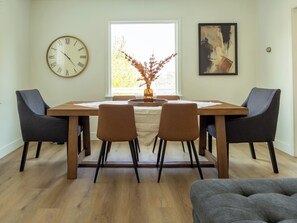 A dining area with a wooden table, four chairs, a clock, a vase with dried plants, and a painting on the wall. - Game Day Getaway - 4BR/3BA, Sleeps 10, Walk to WSU (Pullman)
