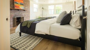 A bedroom with a brick fireplace, a bed with pillows, a bedside table, and a window. - Game Day Getaway - 4BR/3BA, Sleeps 10, Walk to WSU (Pullman)