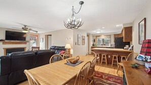 A modern living room with a large flat-screen TV, a fireplace, a leather sofa, and a dining area with wooden chairs and a table. - Sagamore by Avantstay Heated Pool + Game Room Near Gore + Main St (North Creek)