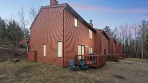 A large, single-story wooden house with a deck, two chairs, and a small table. - Sagamore by Avantstay Heated Pool + Game Room Near Gore + Main St (North Creek)
