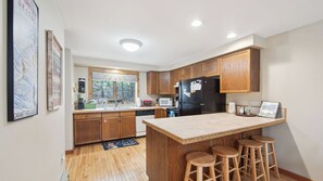 A kitchen with wooden cabinets, a black refrigerator, a microwave, and a sink. - Sagamore by Avantstay Heated Pool + Game Room Near Gore + Main St (North Creek)