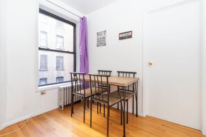 A small dining area with a wooden table and four chairs, a window with a view of buildings, a radiator, and a door. - lovely Delightful 2-bedroom in the upper east side (New York)