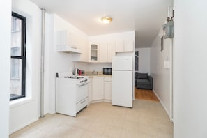 A compact kitchen with white cabinets, a stove, a refrigerator, and a microwave. - lovely Delightful 2-bedroom in the upper east side (New York)