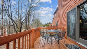 A wooden deck with a table and chairs, a glass door, and a view of trees and buildings. - Chatiemac by Avantstay Wood Fireplace + Resort Pool + Game Room Ski Retreat (North Creek)